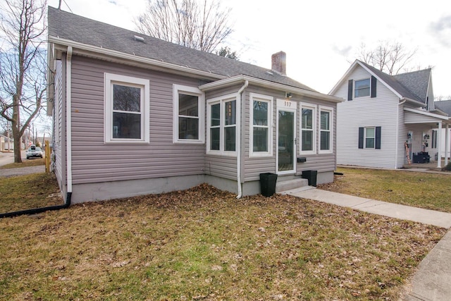 rear view of house with entry steps, a shingled roof, a chimney, and a lawn