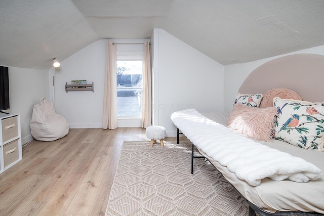 bedroom featuring lofted ceiling, baseboards, a textured ceiling, and light wood finished floors