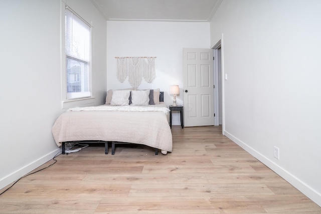 bedroom with ornamental molding, light wood-type flooring, and baseboards