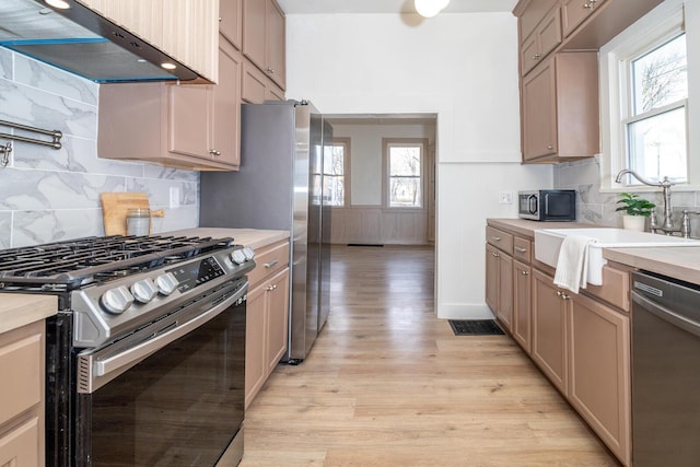 kitchen featuring stainless steel appliances, light countertops, light wood-type flooring, under cabinet range hood, and a sink