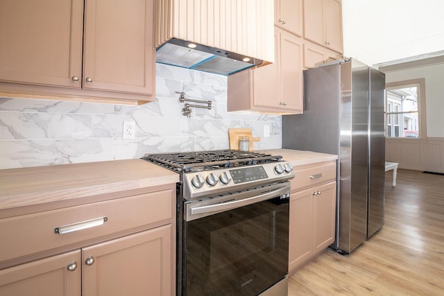 kitchen with light wood-style flooring, under cabinet range hood, stainless steel appliances, light countertops, and tasteful backsplash