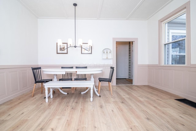 dining area with light wood-type flooring, visible vents, a notable chandelier, and wainscoting