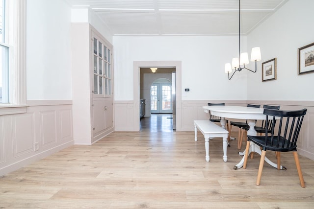 dining area with a wainscoted wall, light wood finished floors, and french doors