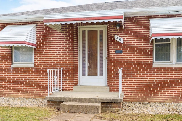 entrance to property featuring brick siding and roof with shingles