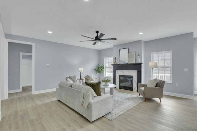 living area featuring recessed lighting, light wood-style flooring, a premium fireplace, a ceiling fan, and baseboards