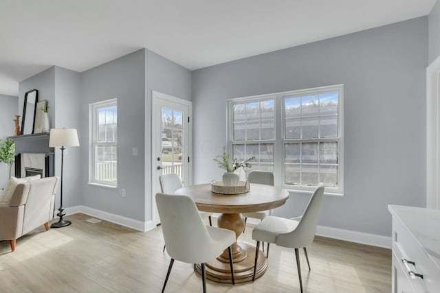 dining room featuring light wood-style floors, a fireplace, and baseboards