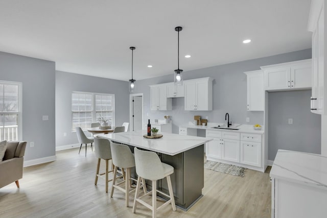 kitchen featuring light wood-style floors, white cabinets, a kitchen island, a sink, and baseboards