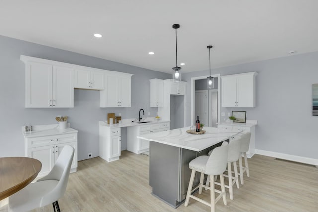 kitchen featuring a center island, a breakfast bar area, light wood-style flooring, white cabinets, and a sink