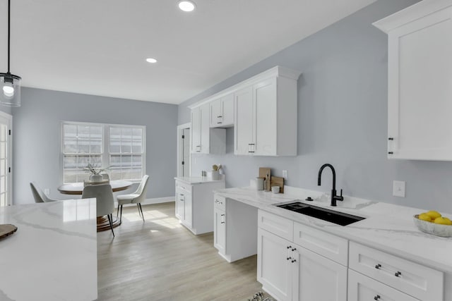 kitchen with white cabinetry, a sink, light wood-style flooring, and light stone countertops