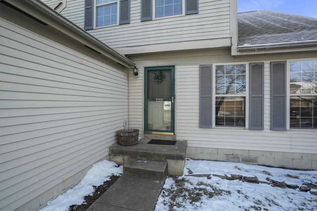 snow covered property entrance with roof with shingles