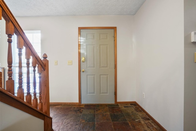 foyer entrance featuring stairs, stone finish flooring, a textured ceiling, and baseboards