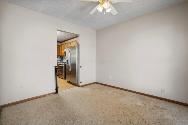 empty room featuring a ceiling fan, baseboards, a textured ceiling, and light colored carpet