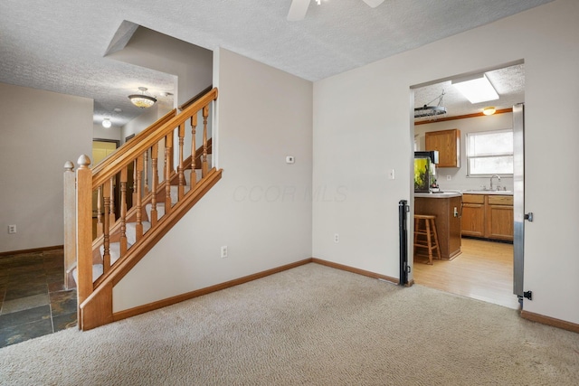 unfurnished room featuring light colored carpet, stairway, a sink, a textured ceiling, and baseboards