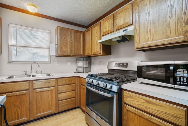 kitchen with stainless steel appliances, light countertops, a sink, a textured ceiling, and under cabinet range hood