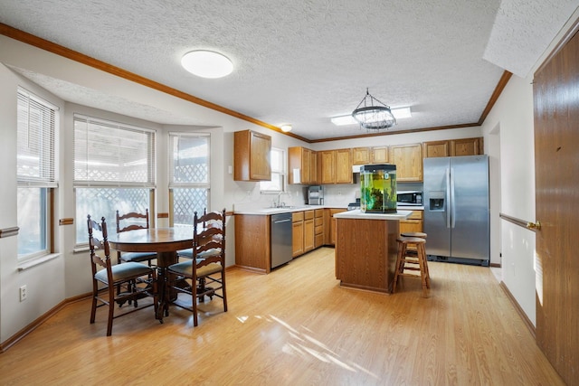 kitchen with crown molding, light wood finished floors, light countertops, appliances with stainless steel finishes, and a kitchen island