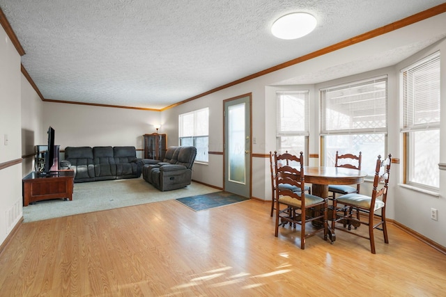 dining space featuring light wood-type flooring, crown molding, a textured ceiling, and baseboards