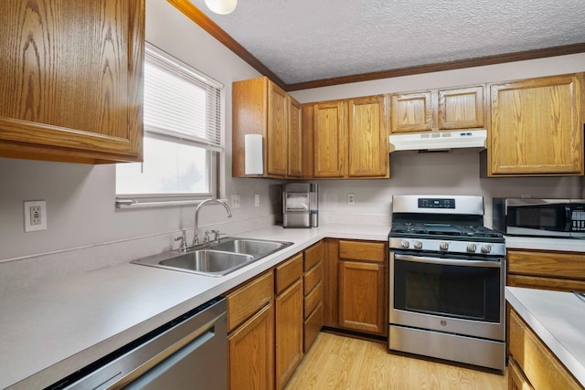 kitchen with appliances with stainless steel finishes, light countertops, a textured ceiling, under cabinet range hood, and a sink