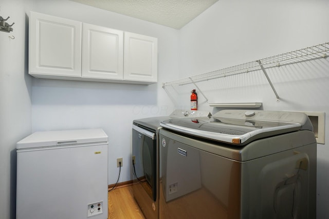 washroom with a textured ceiling, baseboards, light wood-style floors, cabinet space, and washing machine and clothes dryer