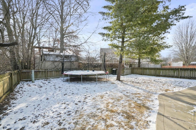 snowy yard with a fenced backyard and a trampoline