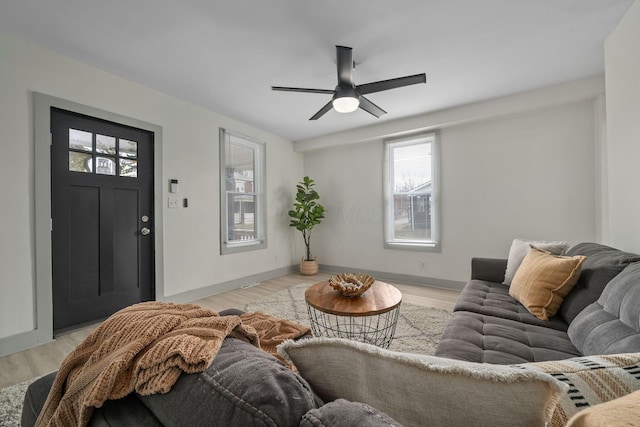 living area with a ceiling fan, light wood-type flooring, and baseboards