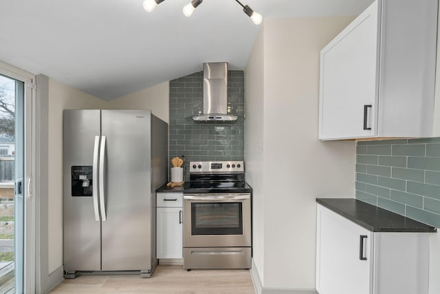 kitchen with dark countertops, wall chimney range hood, white cabinetry, and appliances with stainless steel finishes