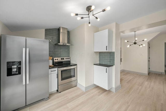 kitchen featuring stainless steel appliances, light wood-type flooring, wall chimney exhaust hood, dark countertops, and an inviting chandelier