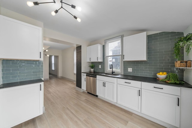 kitchen featuring white cabinets, dark countertops, stainless steel dishwasher, light wood-style floors, and a sink