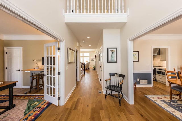 hallway featuring ornamental molding, light wood finished floors, visible vents, and baseboards