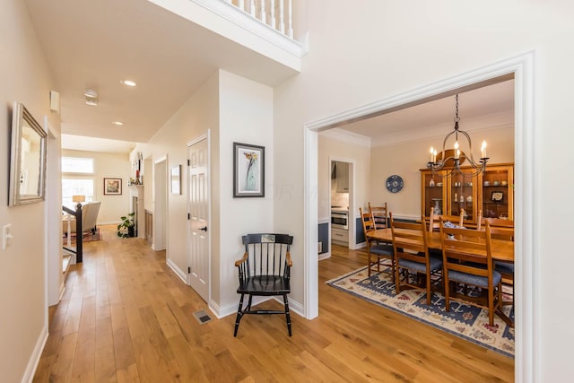 corridor with light wood finished floors, baseboards, visible vents, and an inviting chandelier