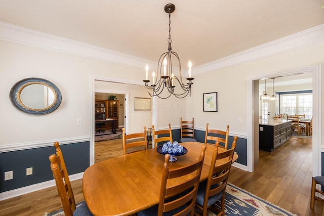 dining area featuring baseboards, ornamental molding, wood-type flooring, and a notable chandelier