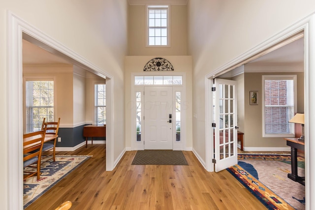 entrance foyer with baseboards, a healthy amount of sunlight, a towering ceiling, and light wood-style floors