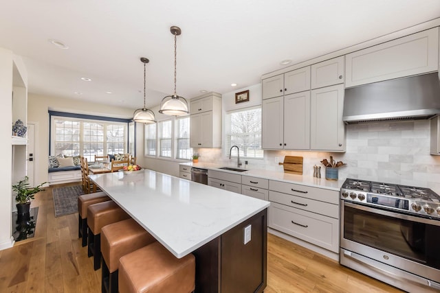 kitchen with stainless steel appliances, gray cabinets, a sink, wall chimney range hood, and a kitchen island