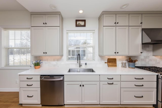 kitchen featuring appliances with stainless steel finishes, gray cabinets, a sink, and wall chimney range hood