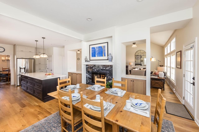 dining room with light wood-style floors, vaulted ceiling, a notable chandelier, and a high end fireplace