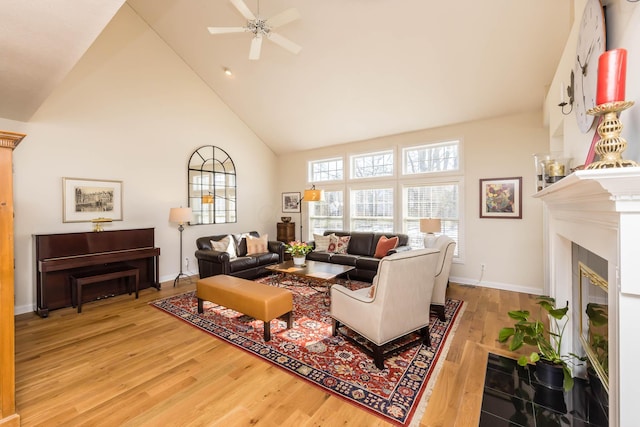 living area with baseboards, a ceiling fan, a fireplace with flush hearth, wood finished floors, and high vaulted ceiling