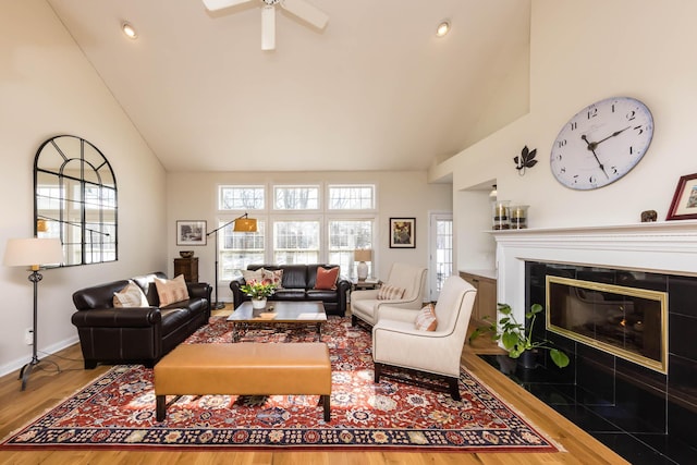 living room featuring high vaulted ceiling, a tiled fireplace, wood finished floors, and baseboards