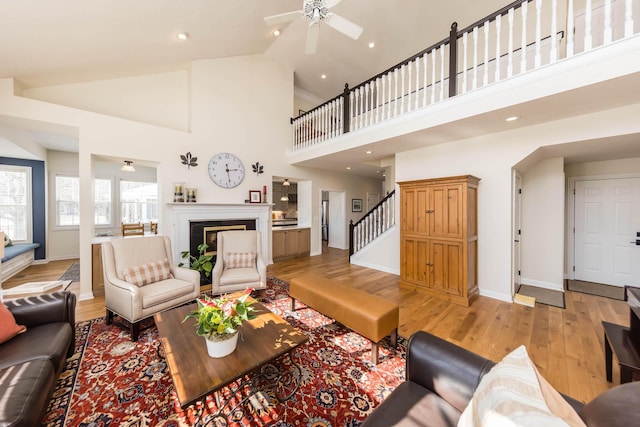 living room featuring light wood-style floors, a glass covered fireplace, high vaulted ceiling, baseboards, and stairs