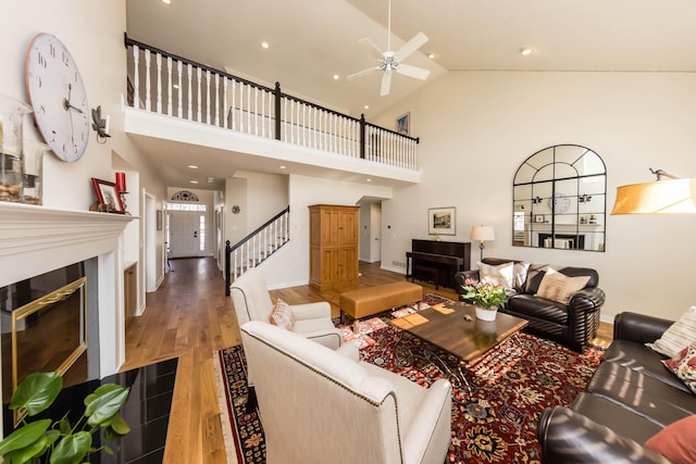 living area featuring ceiling fan, high vaulted ceiling, wood finished floors, stairway, and a glass covered fireplace