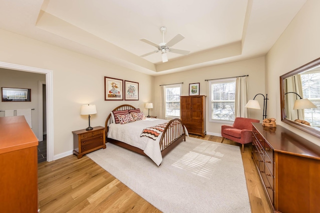 bedroom featuring a tray ceiling, a ceiling fan, light wood-style flooring, and baseboards