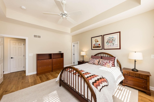 bedroom with a tray ceiling, visible vents, a ceiling fan, wood finished floors, and baseboards