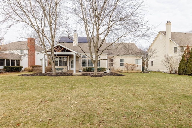 view of front of house featuring roof mounted solar panels, a chimney, and a front lawn