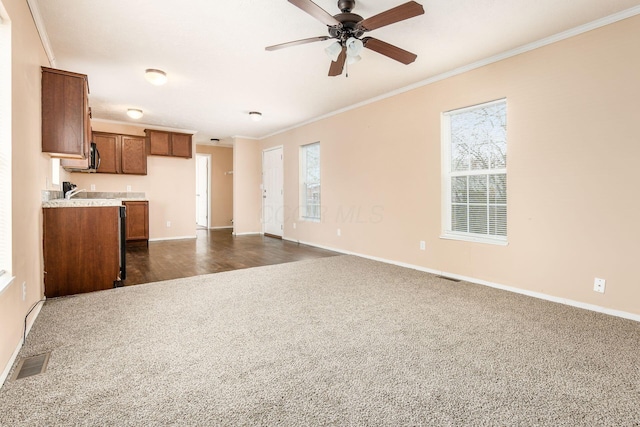 unfurnished living room with plenty of natural light, dark carpet, visible vents, and crown molding