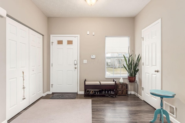 foyer entrance featuring baseboards, a textured ceiling, visible vents, and dark wood-style flooring