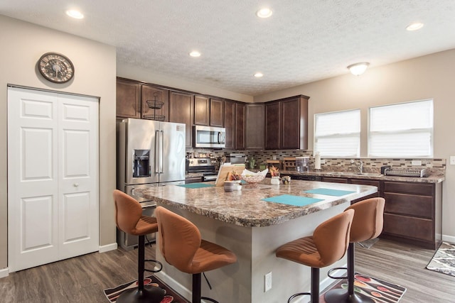 kitchen with appliances with stainless steel finishes, a breakfast bar, backsplash, and dark brown cabinets