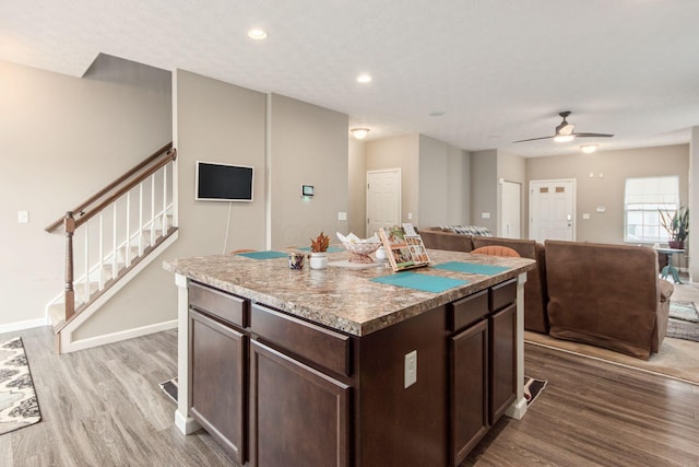 kitchen with a kitchen island, ceiling fan, dark brown cabinets, wood finished floors, and baseboards