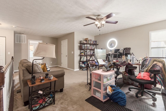 carpeted office space featuring a ceiling fan, baseboards, visible vents, and a textured ceiling