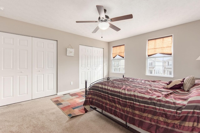 carpeted bedroom with ceiling fan, a textured ceiling, baseboards, and multiple closets