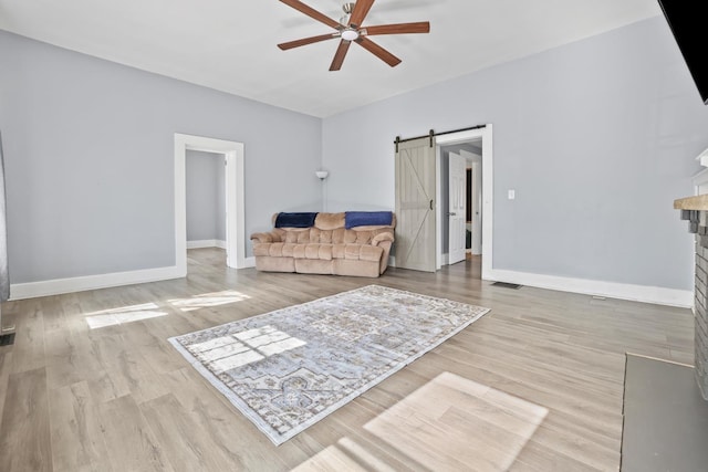 living area featuring a barn door, baseboards, ceiling fan, and wood finished floors