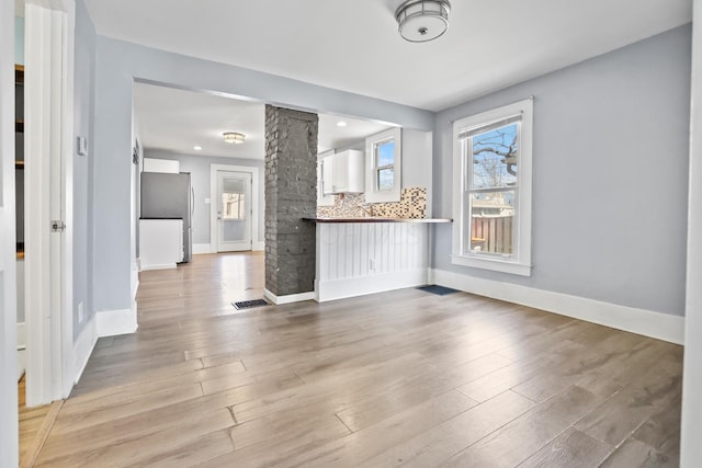 interior space with light wood finished floors, decorative columns, visible vents, and baseboards