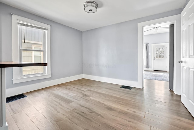 unfurnished room with a wealth of natural light, visible vents, and wood finished floors